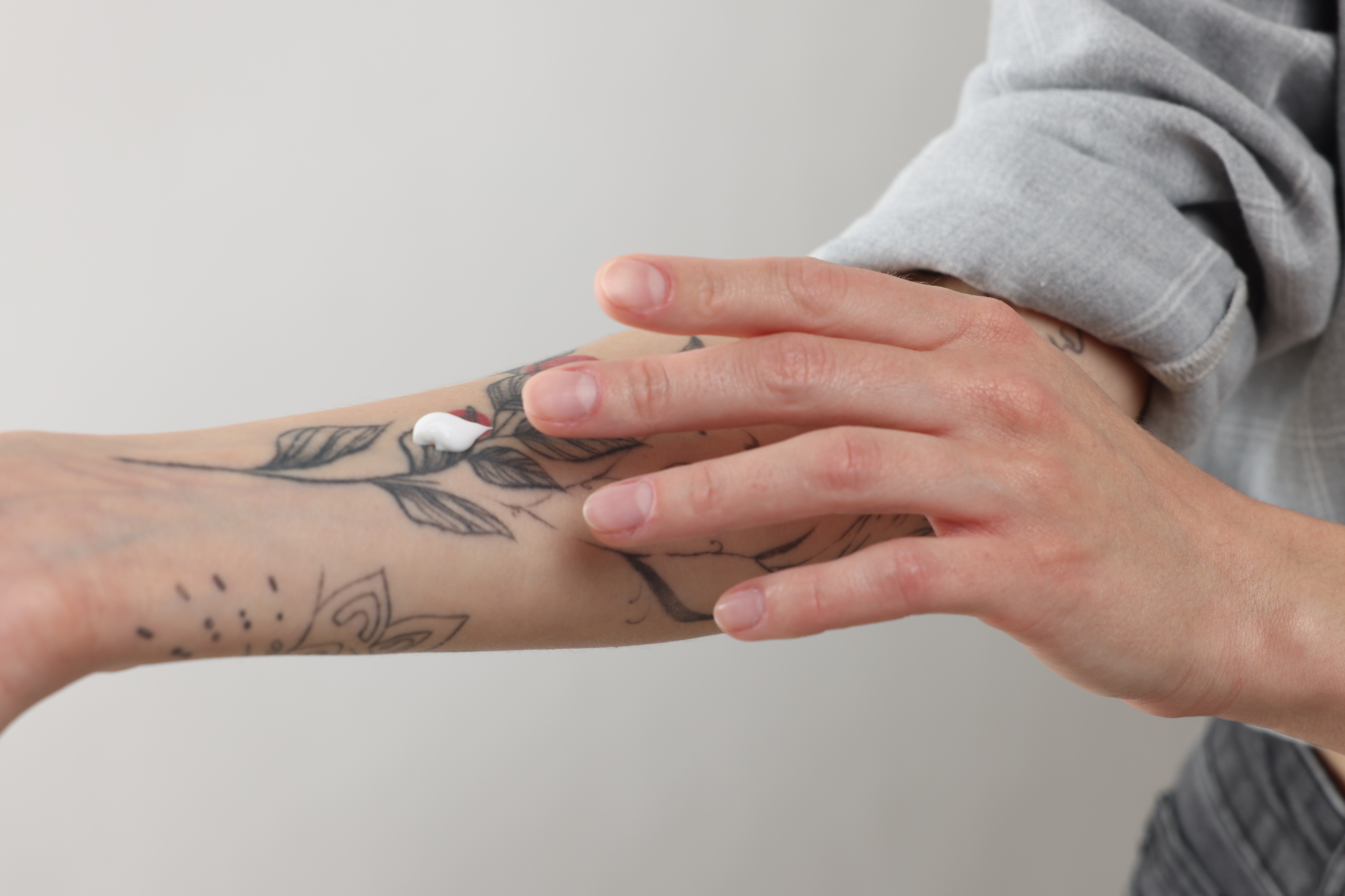 Ženská ruka roztírá krém na potetovaném předloktí